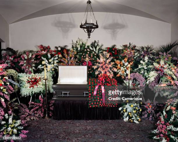 1940s 1950s Open Casket Funeral Home Viewing Parlor Surrounded By Unusual Number Of Fantastic Ornate Floral Bouquet Arrangements