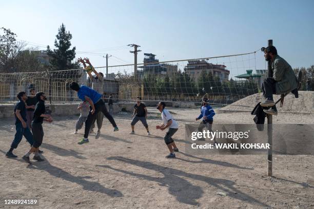 Afghan youth play volleyball as a man sits on the net pole to referee the game in a ground in Kabul on March 21, 2023.