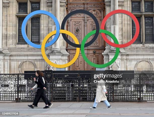 People pass by the Olympic Rings on display in front of the Municipality of Paris, France on March 21, 2023.