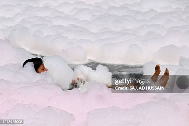 Girl takes a dip in the waters of river Yamuna coated with polluted foam in New Delhi on March 21, 2023.