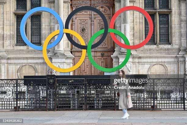 Woman walks past the Olympic Rings on display in front of the Municipality of Paris, France on March 21, 2023.