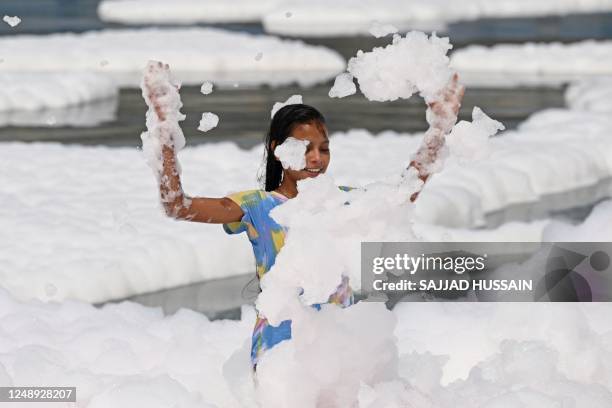 Girl plays in the waters of river Yamuna coated with polluted foam in New Delhi on March 21, 2023.