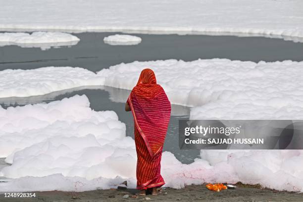 Hindu devotee offers prayers on the banks of river Yamuna coated with polluted foam in New Delhi on March 21, 2023.