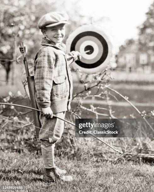 1920s 1930s Proud Smiling Boy Archer Looking At Camera Wearing Knickers Woolen Cap Sweater Pulling Arrow From Target Bulls Eye