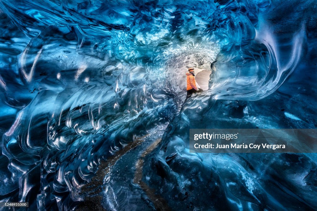 Man ice climber exploring a blue ice cave in Vatnajokull Glacier, Golden Circle Route, Iceland