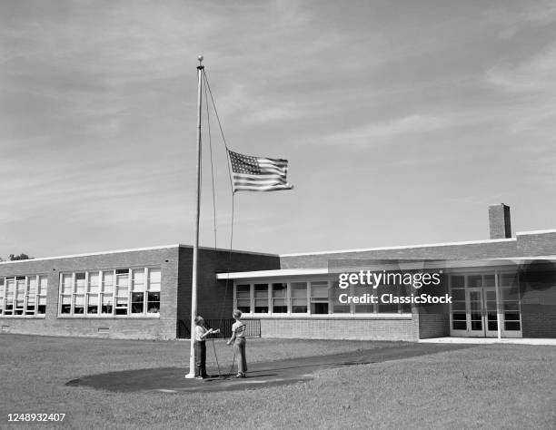 Boy And Girl Raising American Flag In Front Of School Building