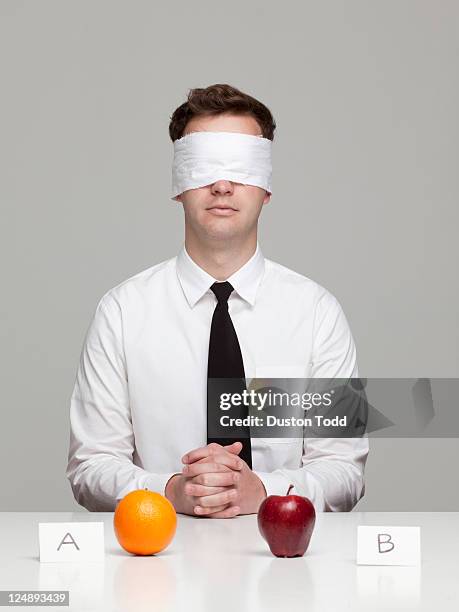 studio portrait of young man with blindfold choosing between orange and apple - choosing experiment stockfoto's en -beelden