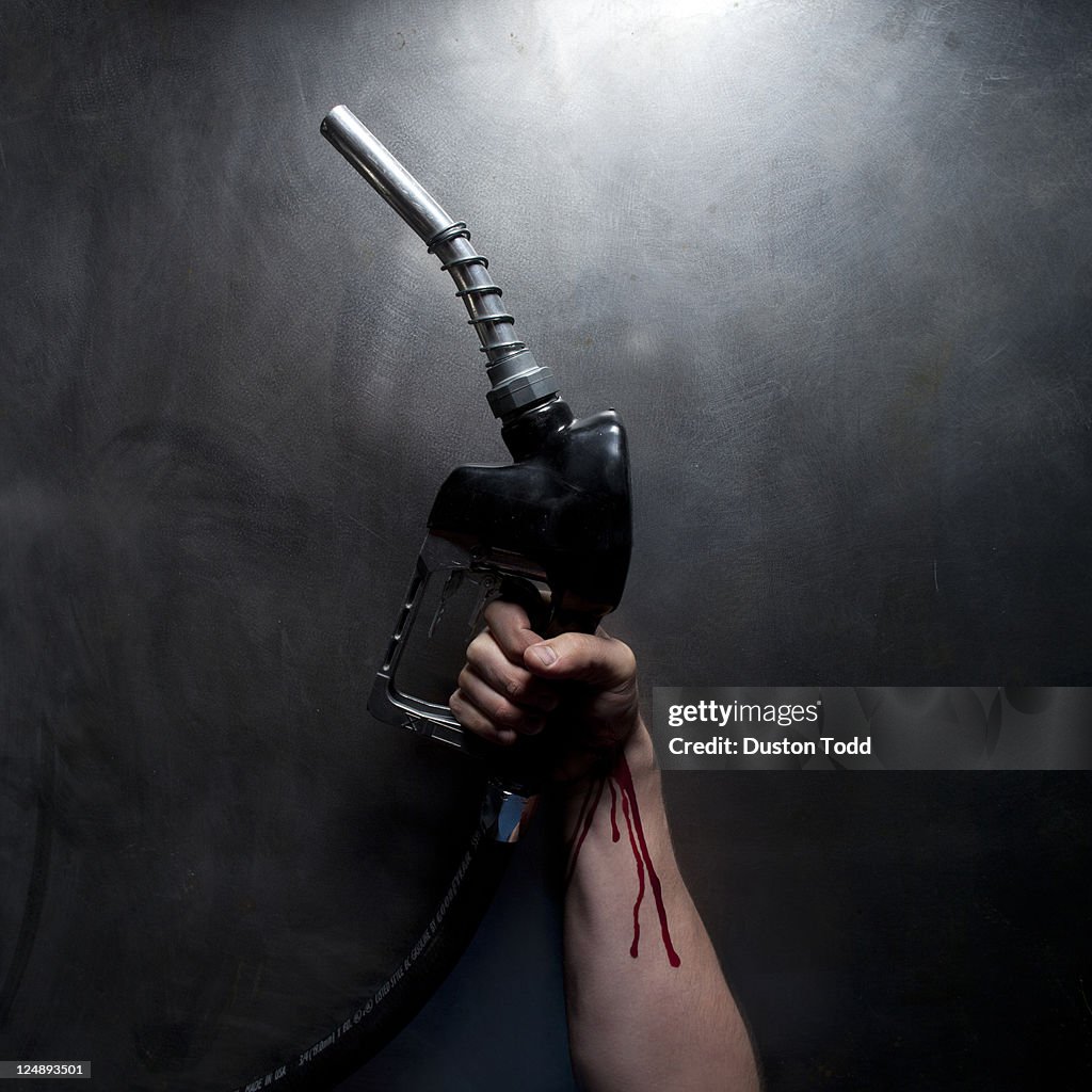 Studio shot of man's hand with blood holding gasoline nozzle