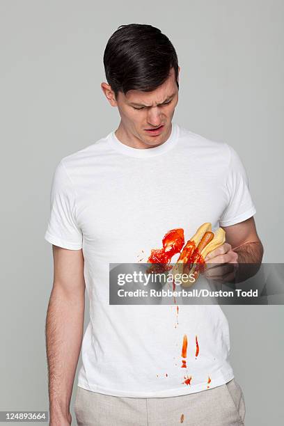 young man wearing stained t-shirt holding hot-dog - tomatenketchup stockfoto's en -beelden