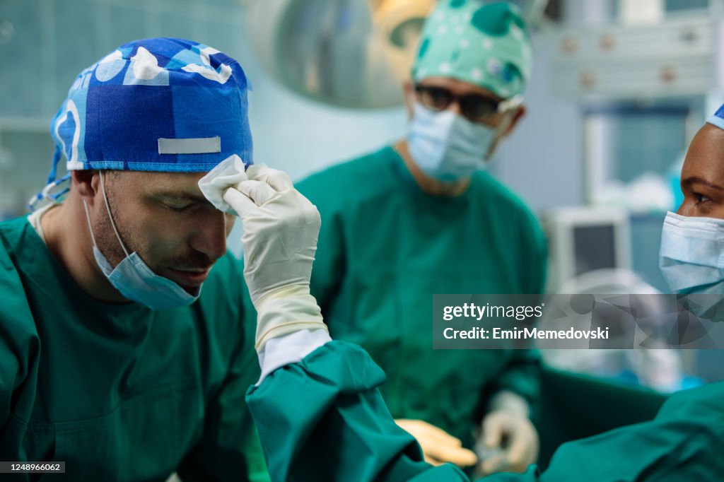 Nurse drying forehead of a surgeon next to a patient in an operating room