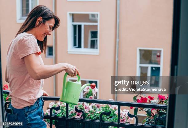 frau kümmert sich um ihre blumen auf dem heimischen balkon. - blumen giessen stock-fotos und bilder