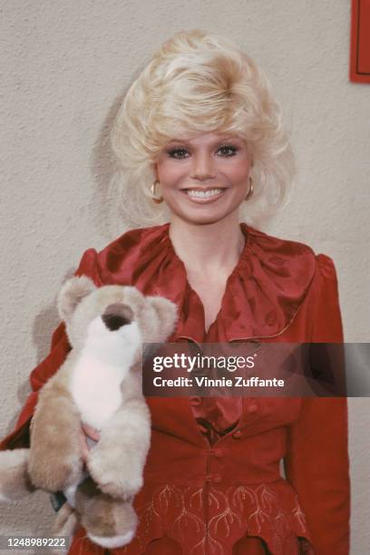 American actress Loni Anderson wearing a red blouse with a shawl collar, holding a soft toy, December 1981.