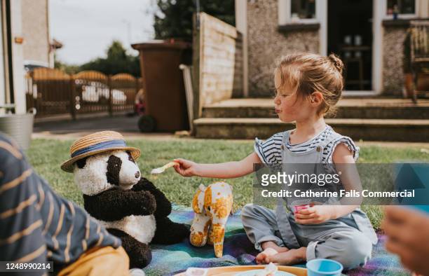 children sit outside and have a teddy bear's picnic - sisters feeding bildbanksfoton och bilder