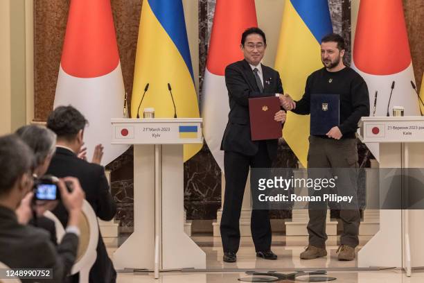 Ukrainian President Volodymyr Zelensky and Japanese Prime Minister Fumio Kishida shake hands while holding signed documents during the joint press...