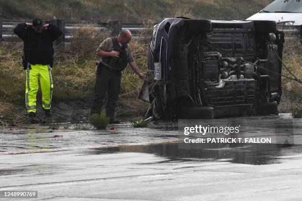 Los Angeles County Sheriffs Department deputy and California Highway Patrol officer look at a flipped vehicle in the rain on Interstate 5 during a...