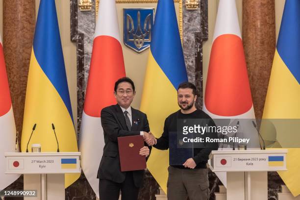 Ukrainian President Volodymyr Zelensky and Japanese Prime Minister Fumio Kishida shake hands while holding signed documents during the joint press...