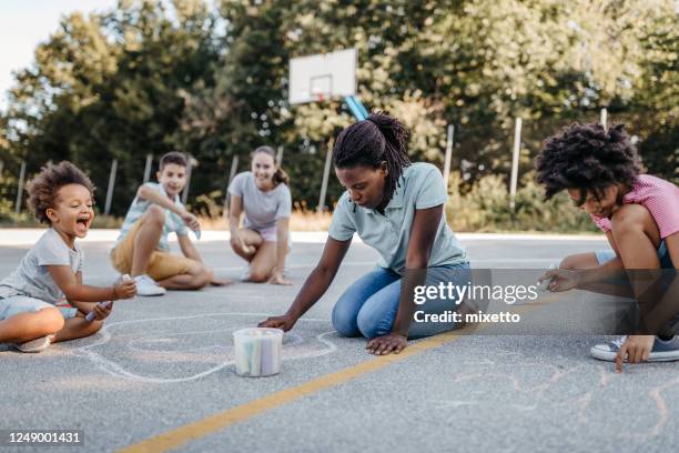 children with women drawing on playground using chalk - family chalk drawing stock pictures, royalty-free photos & images