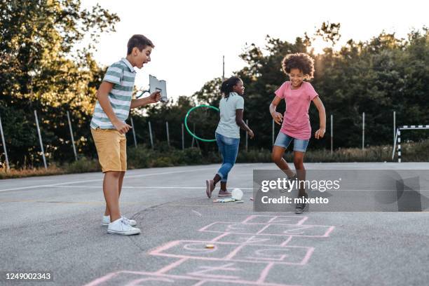 mother holding plastic hoop while children playing hopscotch - hopscotch stock pictures, royalty-free photos & images