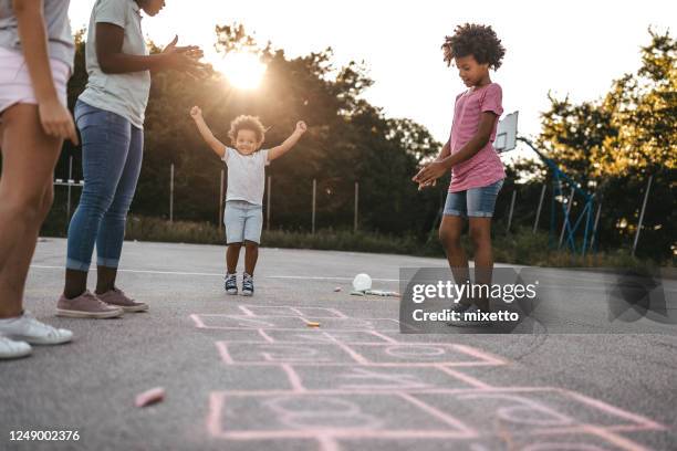 mother encouraging children playing hopscotch - hopscotch stock pictures, royalty-free photos & images