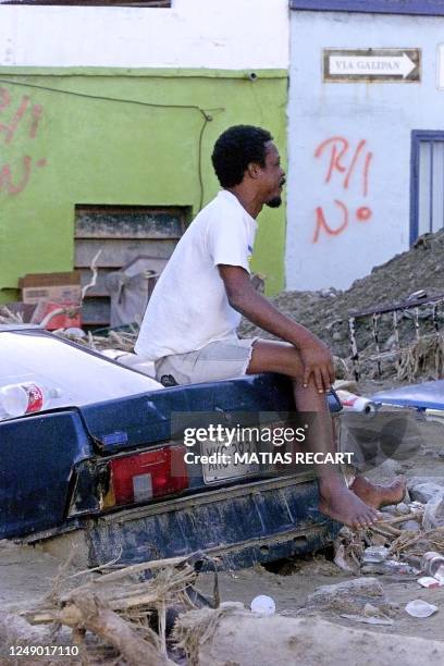 Resident of La Guaira takes a break 25 December among the destruction left by floods. Un hombre descanza sentado arriba de un auto sepultado por el...