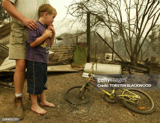 William Snare is comforted by his stepfather Chris Pye as he finds the burnt remains of his new bicycle in the ruins of their home after a firestorm...