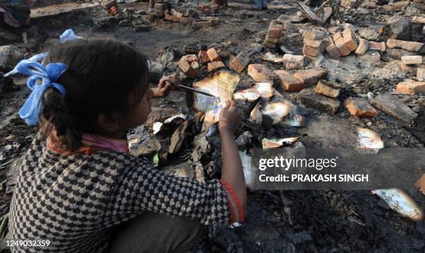 Kavita salvages her school text books as she sits near the remains of her smouldering hut in New Delhi on January 31, 2012. Score of slum huts were...