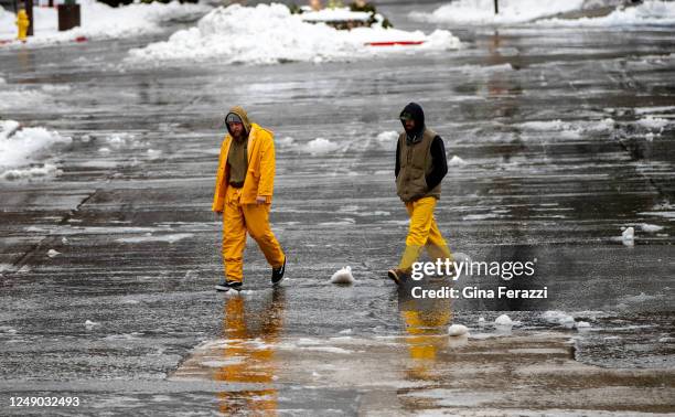 Workers dressed in rain gear walk across the slushy parking lot at Lake Arrowhead Village as sleet falls on the mountain community on March 21, 2023...