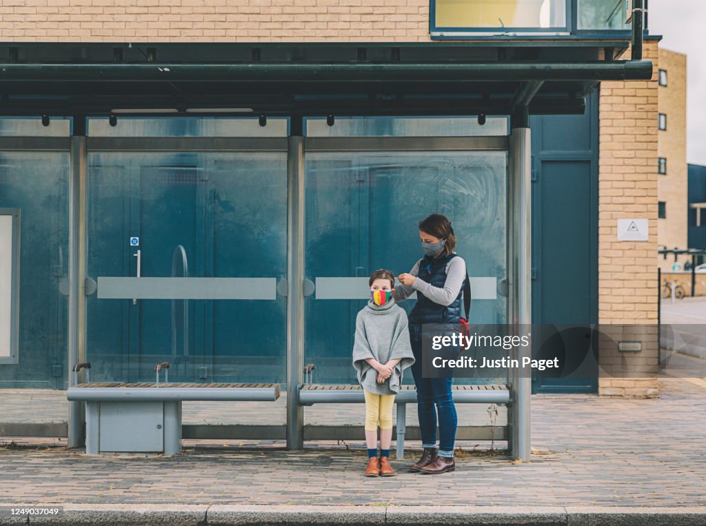Young girl and her mother waiting for the bus. They both wear masks
