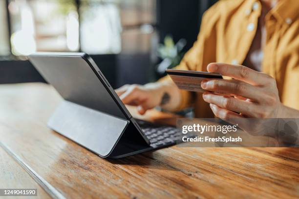 hombre usando una tarjeta de crédito para comprar en línea en su tableta digital - comercio electrónico fotografías e imágenes de stock