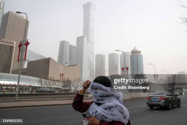 Pedestrian covers her face with a scarf while walking along a road shrouded in smog during a sandstorm in Beijing, China, on Wednesday, March 22,...