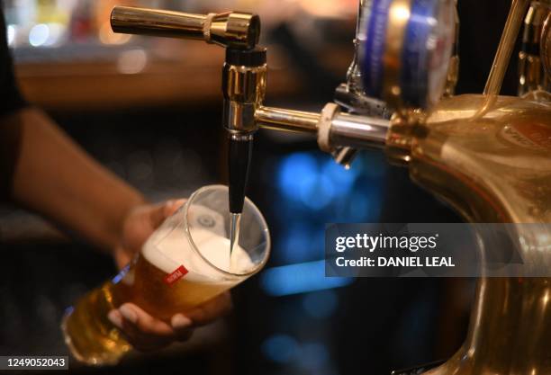 In this file photo taken on November 30, 2022 an employee pours a pint of Peroni beer on at the bar in the Mad Hatter pub and hotel in London. -...