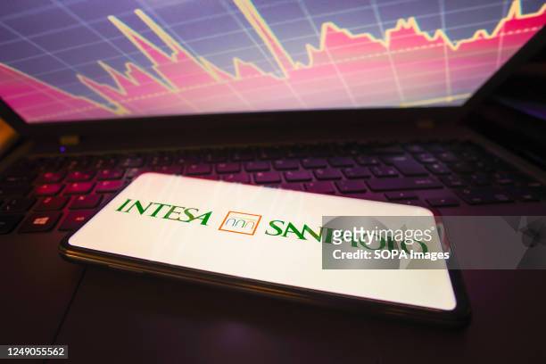 In this photo illustration the Intesa Sanpaolo logo seen displayed on a smartphone screen, with graphic representation of the stock market in the...