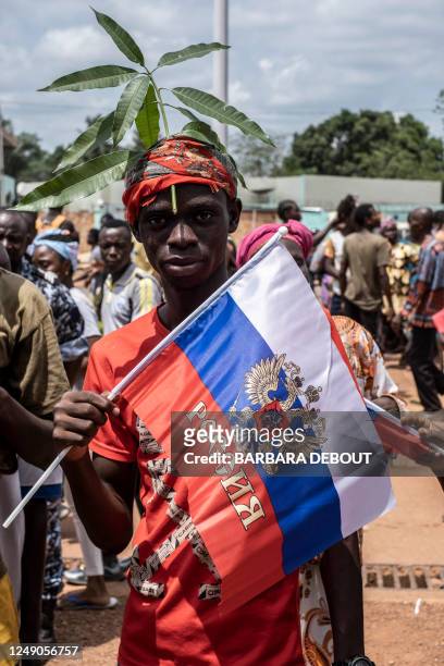 Demonstrator with foliage on to his head, a sign of compassion in Central African Republic, holds a Russian flag with the emblem of Russia on while...