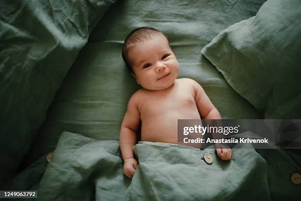 top view and close-up portrait of cute adorable naked baby girl in bedroom. newborn child relaxing and smiling in the green linen parent's bed. family morning at home. - innocence stock pictures, royalty-free photos & images