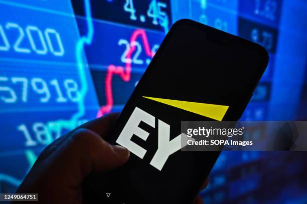 In this photo illustration, an Ernst & Young logo is displayed on a smartphone with stock market percentages in the background.