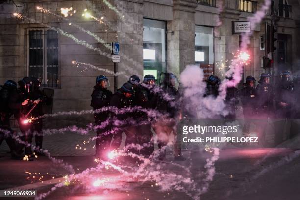 Police officers stand in front of fireworks fired by protesters during a demonstration, a few days after the government pushed a pensions reform...