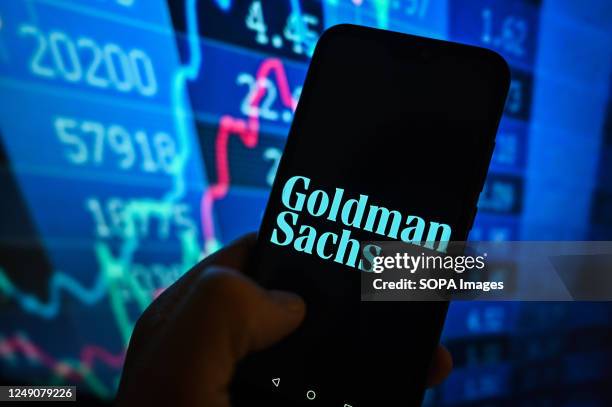In this photo illustration, a Goldman Sachs logo is displayed on a smartphone with stock market percentages in the background.
