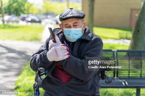 portrait of the senior 90-years-old man wearing a protective mask and gloves because of the covid-19 pandemic, talking with his family using a smartphone. - alex potemkin coronavirus stock pictures, royalty-free photos & images