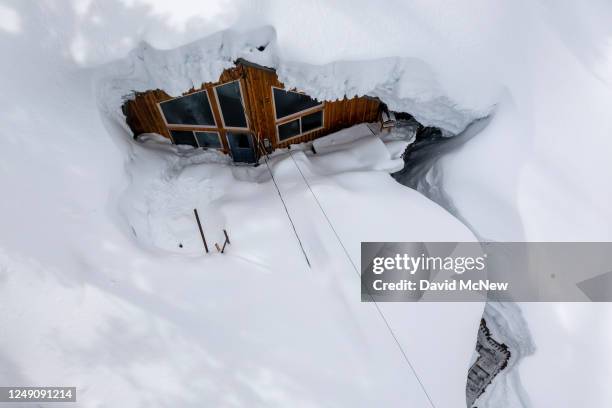 In an aerial view, at the bottom of a deep and narrow trench, a pathway lead up to a house buried in heavy snow as storms continue to increase the...