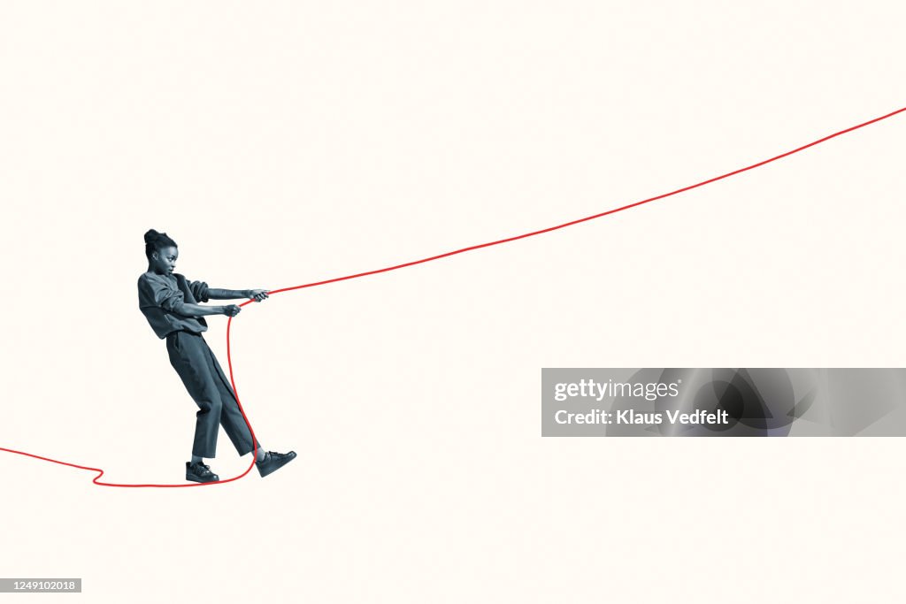 Side view of young woman pulling vibrant red rope
