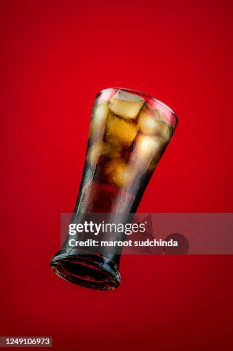Cola in glass and ice cubes detail on red background Cola in glass and ice cubes detail on red background