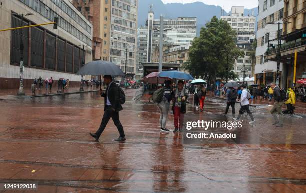 People walk with umbrellas on the sidewalk during rainfall in Bogota downtown, Colombia on March 22, 2023.