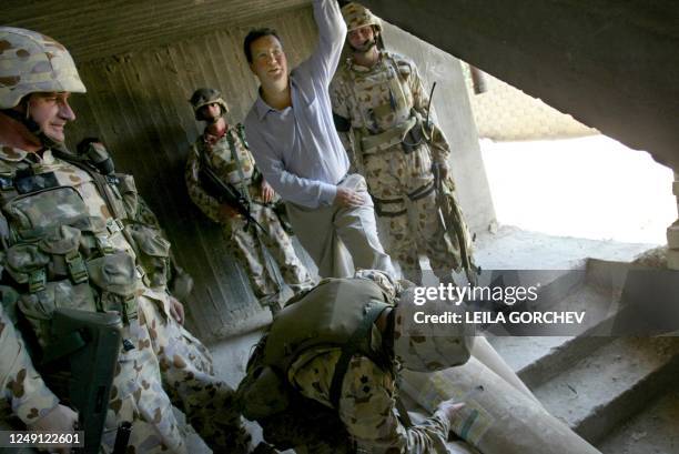 An Australian soldier removes tar from the shoe of Australian Foreign Minister Alexander Downer as they enter an abandoned building next to the...
