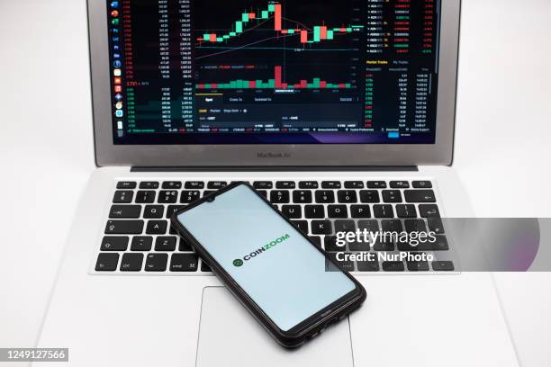 In this photo illustration a CoinZoom logo seen displayed on a smartphone screen and an Exchange graph on a MacBook screen in Athens, Greece on March...