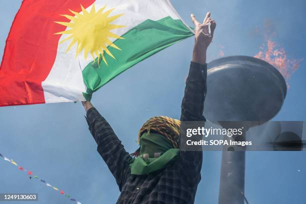 Young man with his face covered holding the Iraqi Federal Kurdistan flag poses in front of the Newroz fire during the celebration. At the call of the...