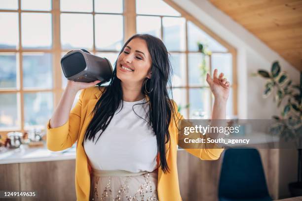 frau tanzt zu hause, während sie drahtlose lautsprecher hält - bluetooth speaker stock-fotos und bilder