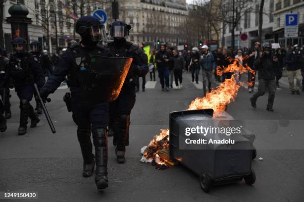 Riot police walk past a garbage set on fire by demonstrators during a protest against the government after pushing the pensions reform without a vote...
