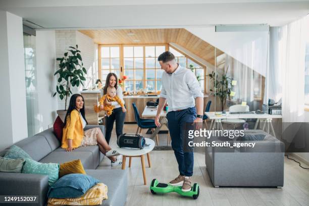 リビングルームでホバーボードに乗っている間、男は彼の家族を楽しませます - hover board ストックフォトと画像
