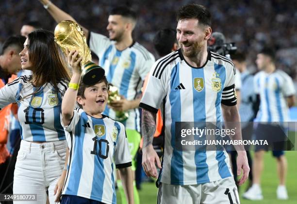 Argentina's forward Lionel Messi looks at his son Thiago as he raises a replica of the World Cup trophy during a recognition ceremony for the World...