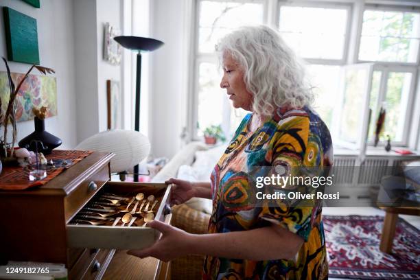 senior woman wearing colorful at home opening drawer with precious cutlery - cómoda imagens e fotografias de stock